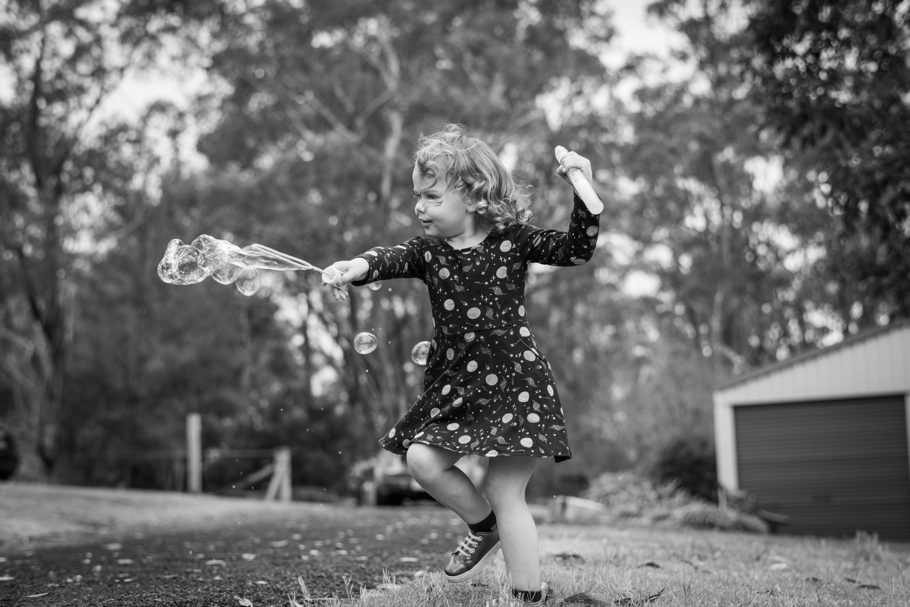 A young girl in a spotted dress twirling on a lawn, arms out, in soft afternoon light