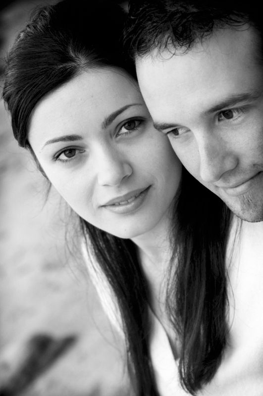 A couple cheek to cheek looking into the camera, in black and white