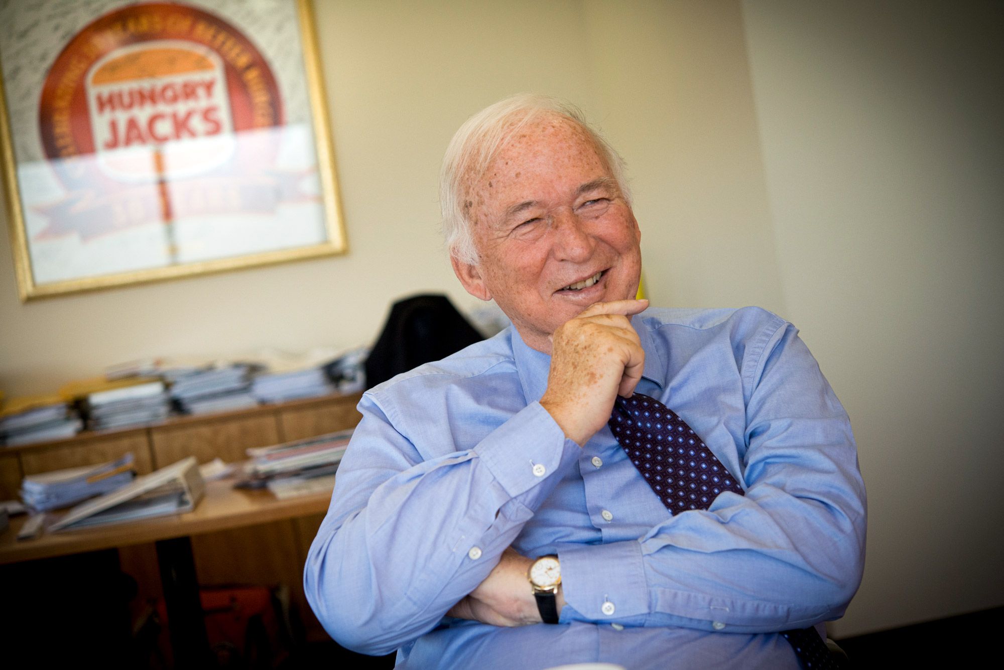 An older man in a blue shirt laughing in his office