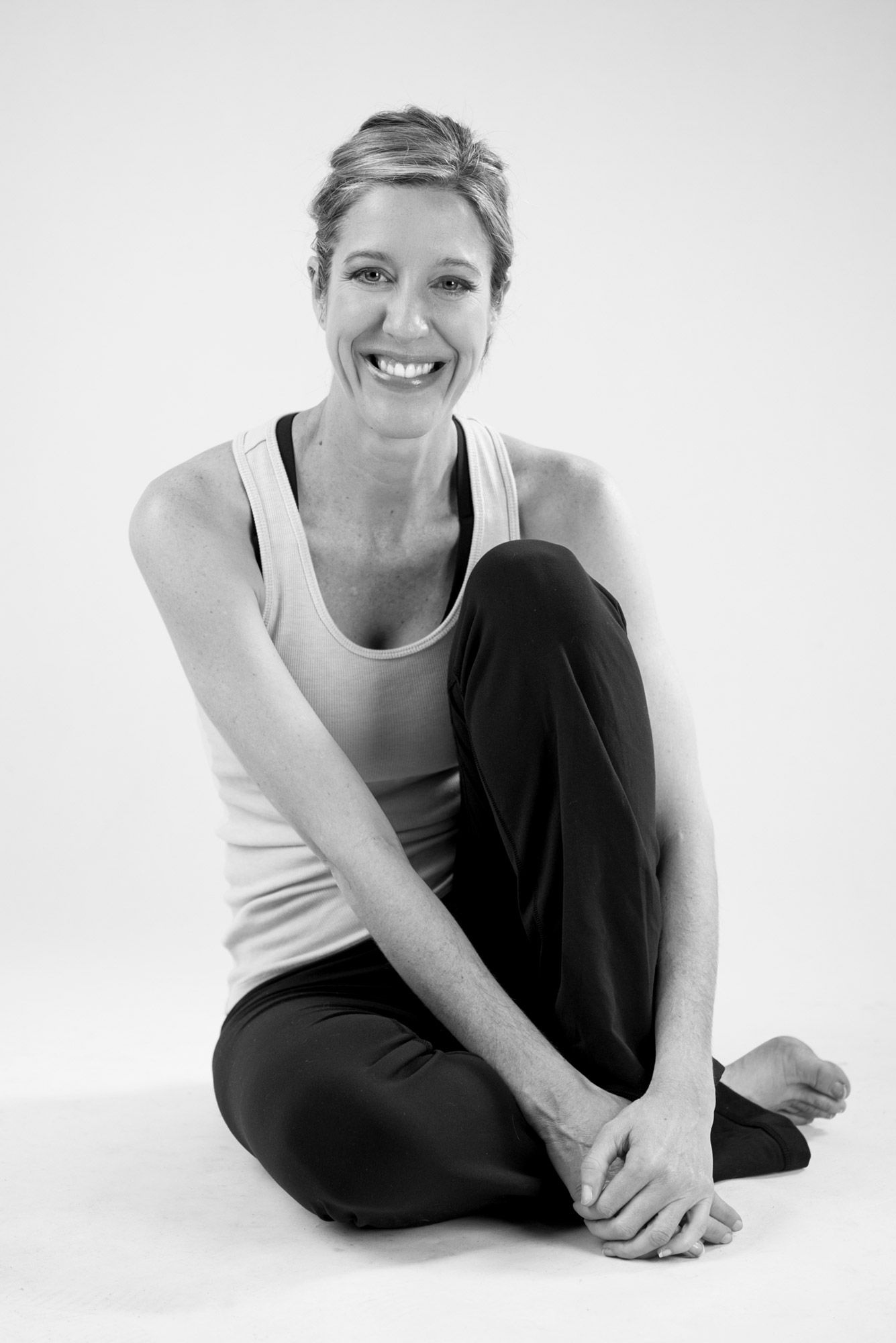 A woman seated with her arms around her knees, in black and white