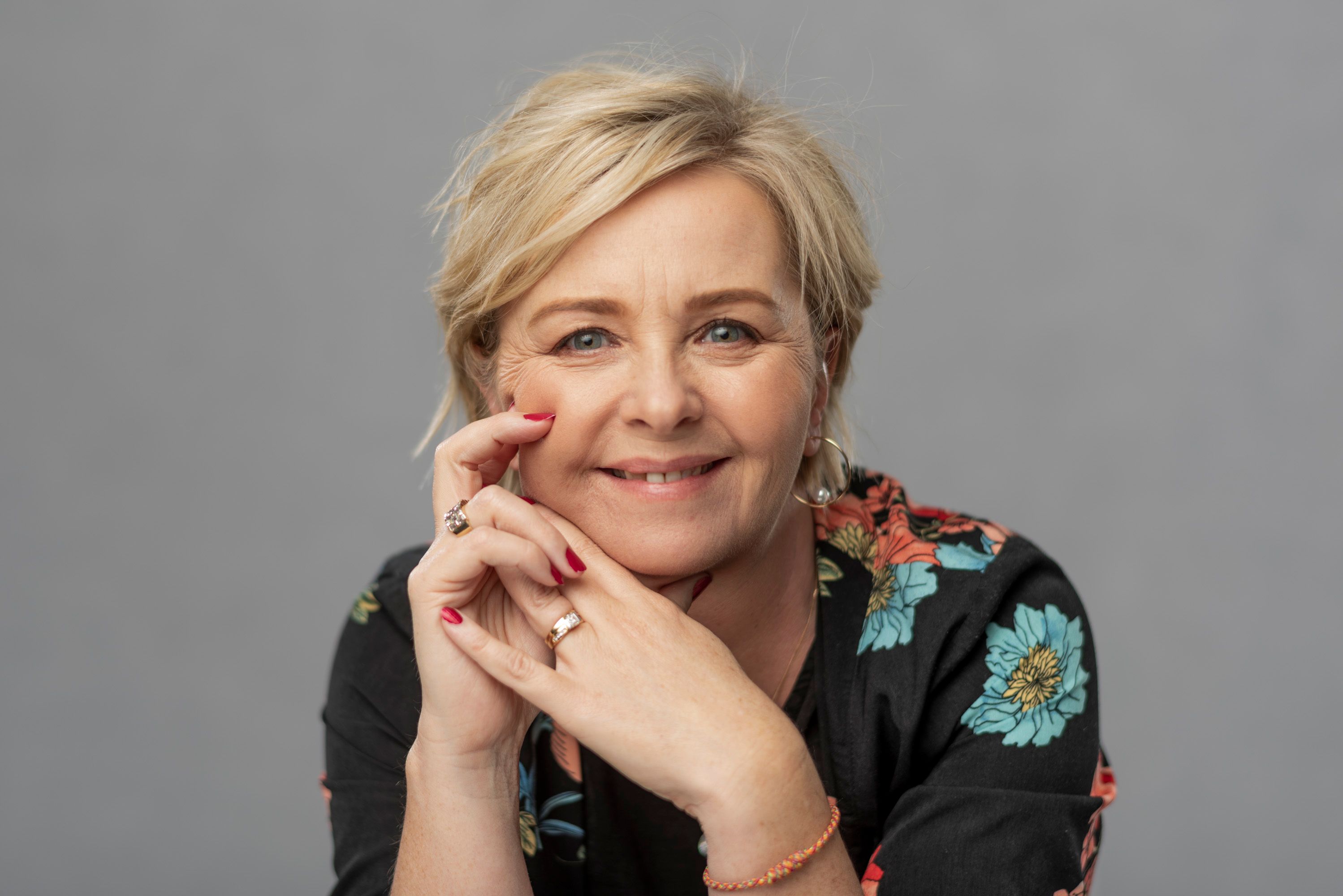 A woman in a floral top smiling warmly with her hand to her cheek