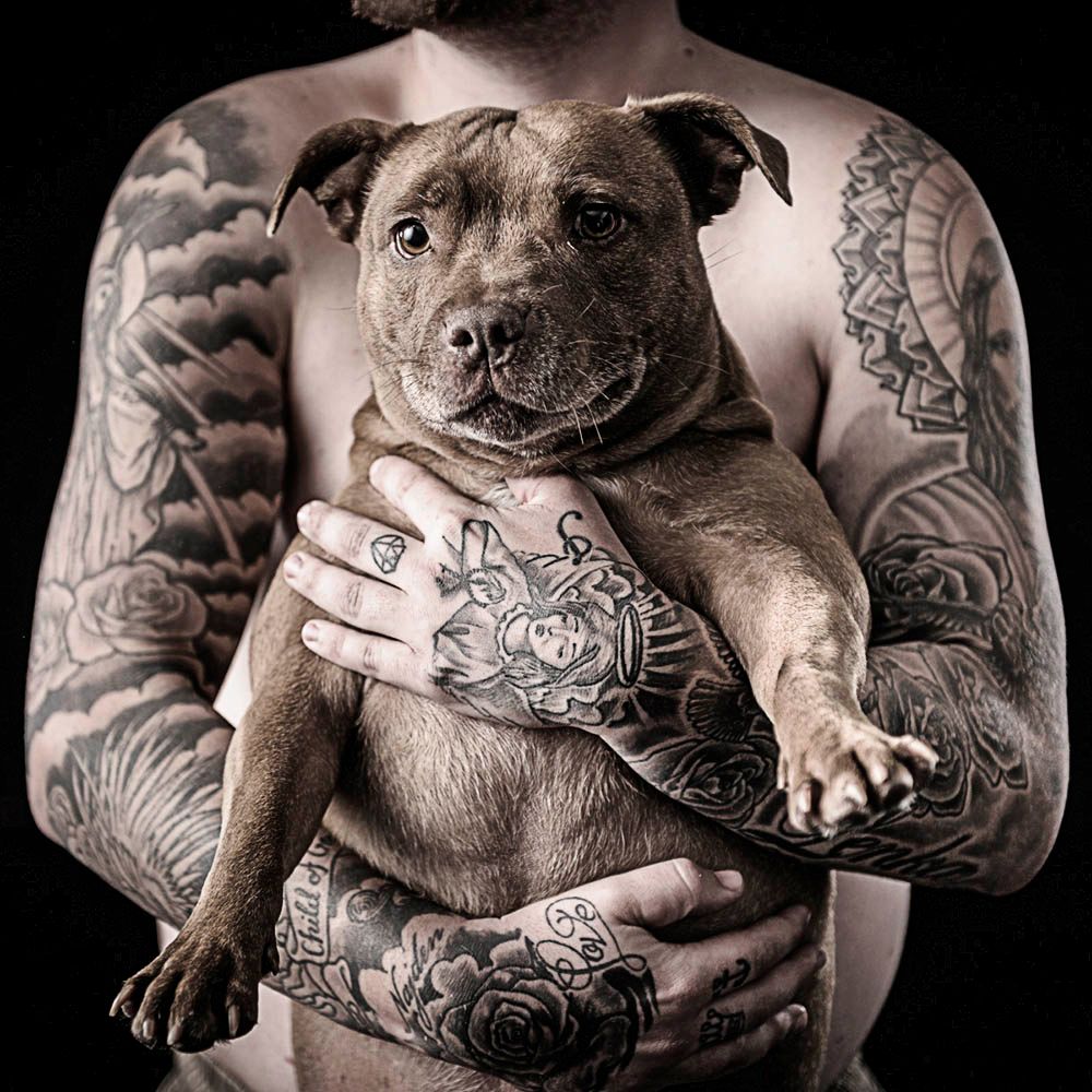 A tattooed owner cradling a grey Staffordshire terrier, in black and white